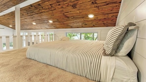 A bedroom with a wooden ceiling, a large bed with striped bedding, and a view of greenery outside. - Secluded Bluebell Cottage with Private Fire Pit! (Menlo)