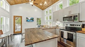 A modern kitchen with white cabinetry, a wooden ceiling, and a large island with a built-in oven. - Secluded Bluebell Cottage with Private Fire Pit! (Menlo)