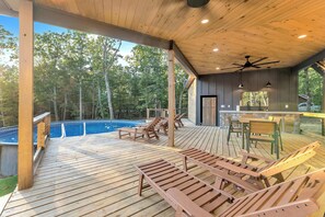 A covered outdoor deck with wooden furniture, a pool, and a stone wall. - Secluded Bluebell Hideaway with Private Fire Pit! (Menlo)
