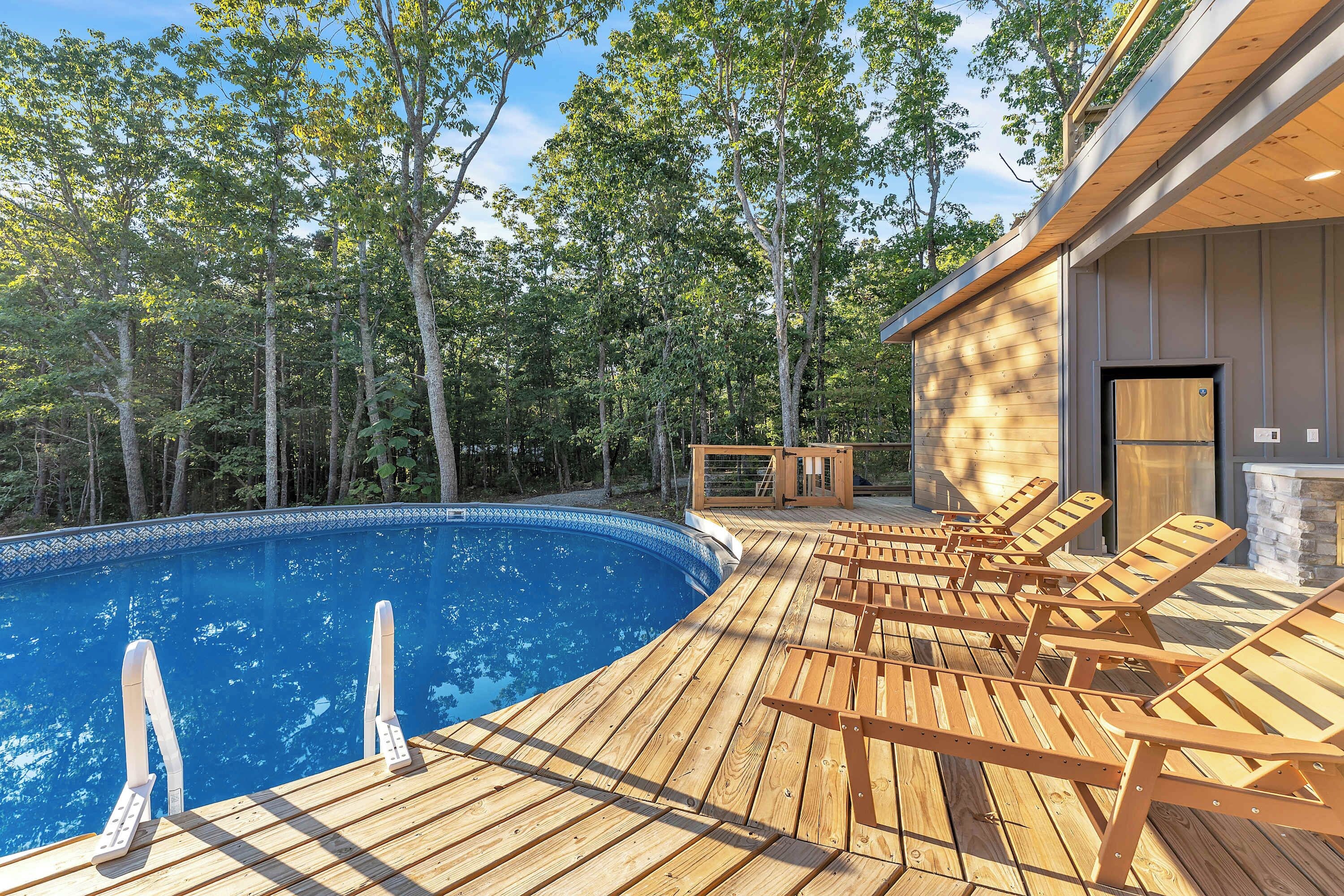 A wooden deck with a pool, lounge chairs, and a stone fireplace.