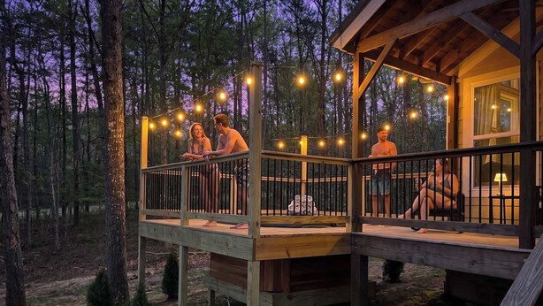 Une terrasse en bois agrémentée de guirlandes lumineuses, un espace salon abrité et une petite table, le tout offrant une vue sur la forêt.