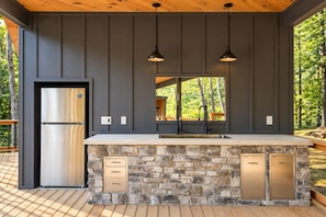 A modern kitchen with a stone island, stainless steel refrigerator, and pendant lighting.