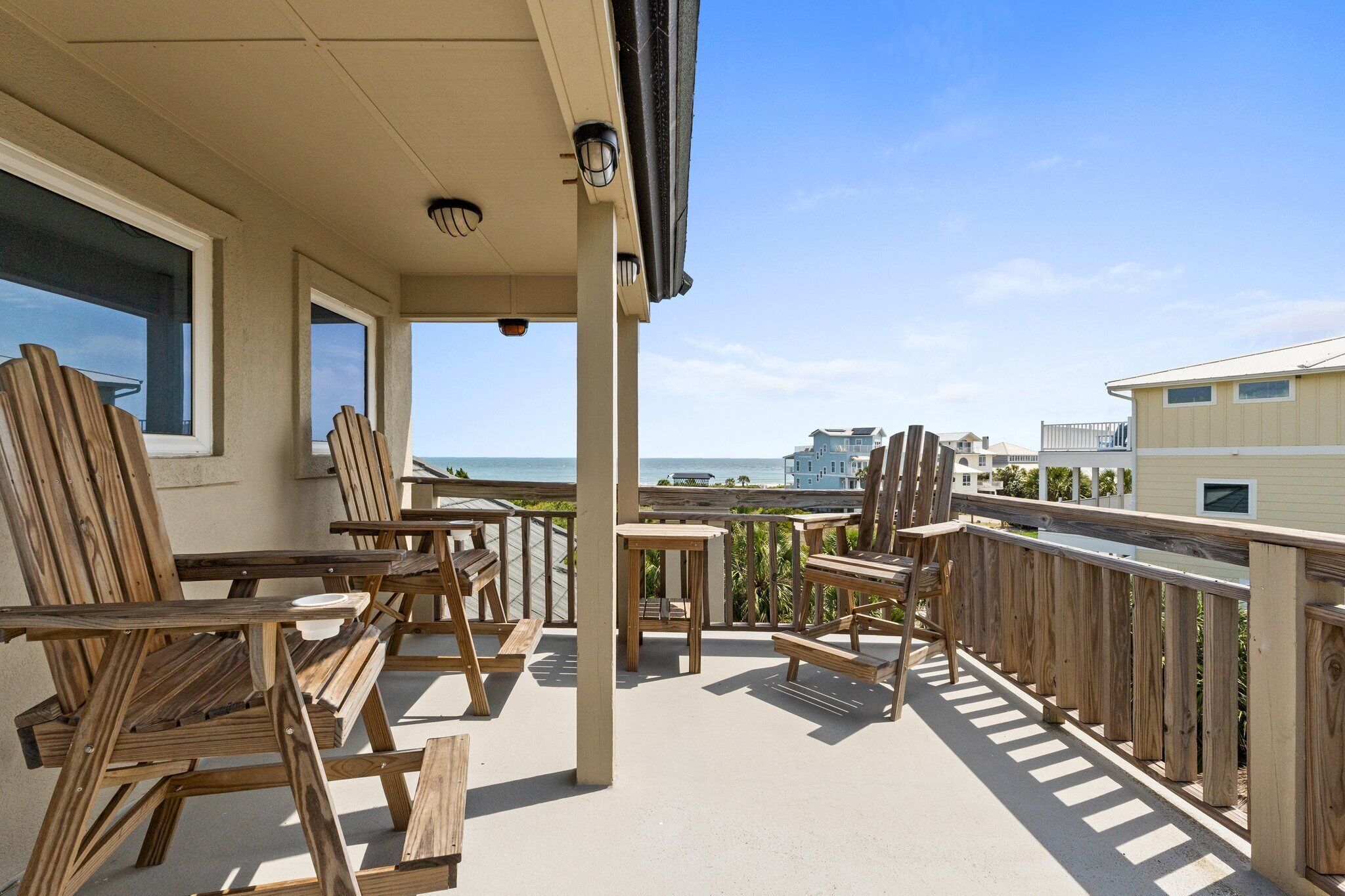 A wooden deck with outdoor furniture, overlooking a beach and ocean.