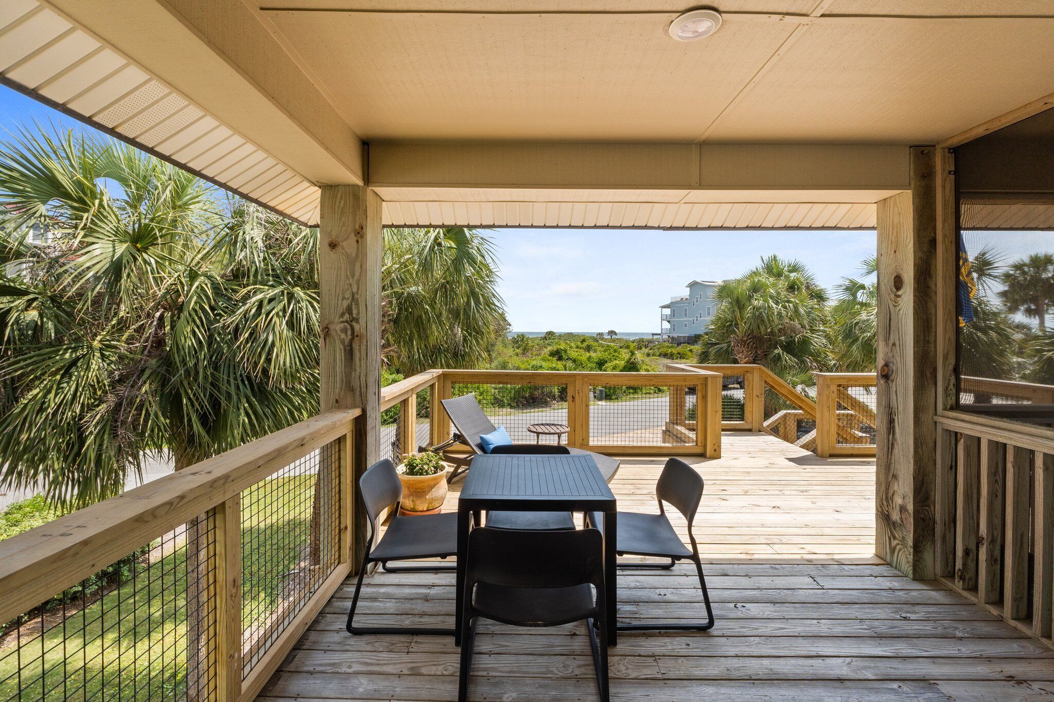 Une terrasse extérieure couverte, dotée d’une table et de chaises, entourée d’une balustrade en bois et de palmiers.