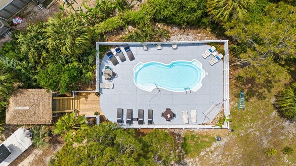 An aerial view of a pool area with lounge chairs, a hot tub, and a wooden deck.