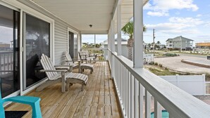 A covered porch with wooden chairs and tables, large sliding glass doors, and a view of the surrounding neighborhood.