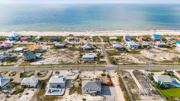 An aerial view of a coastal residential area with houses, roads, and a beach.