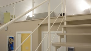 Eine Treppe mit weißen Geländern und einer beigen Wand. Auf dem Zwischenpodest befinden sich Türen und ein kleines Regal mit Gegenständen.