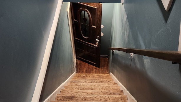 A wooden staircase with a handrail, leading to a door with a circular window. - Muskegon Lake View Loft studio/kitchenette (Muskegon)