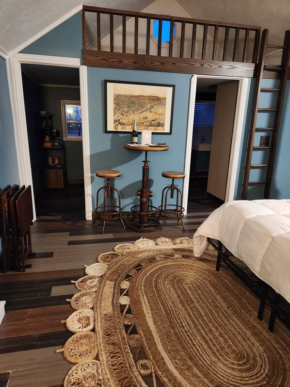 A bedroom with a bunk bed, a round coffee table, two stools, a large rug, and a painting on the wall.