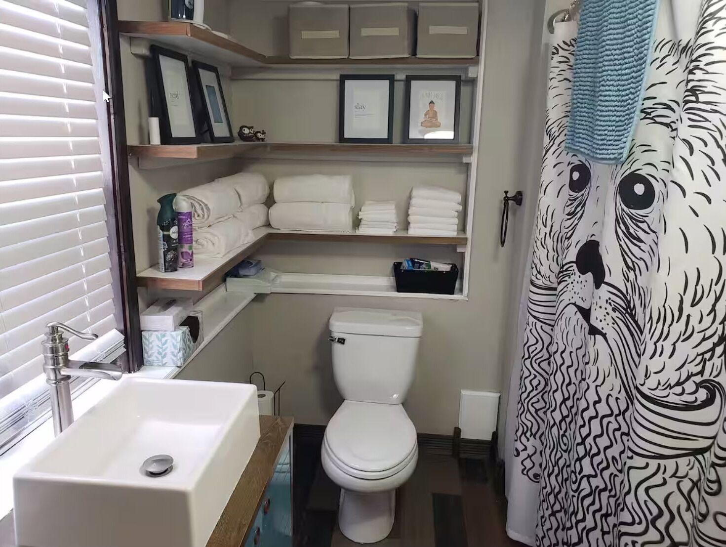 A bathroom with a white sink, toilet, and shelves with towels and toiletries.