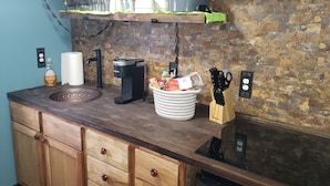 A kitchen with a stone backsplash, wooden cabinets, a coffee maker, and various kitchen utensils. - Muskegon Lake View Loft studio/kitchenette (Muskegon)