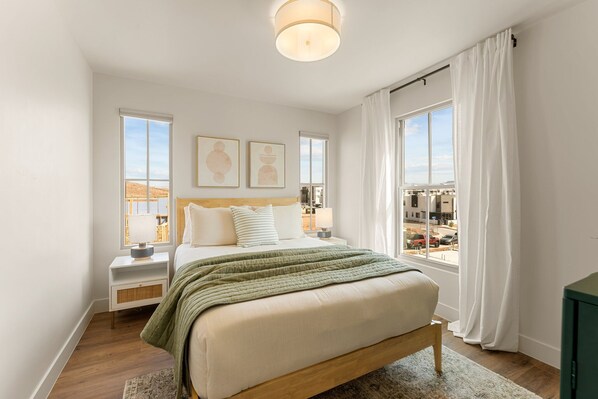 A bedroom with a bed, bedside tables, a window with curtains, and artwork on the wall.