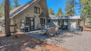 A two-story cabin with a patio area featuring outdoor furniture and a grill.