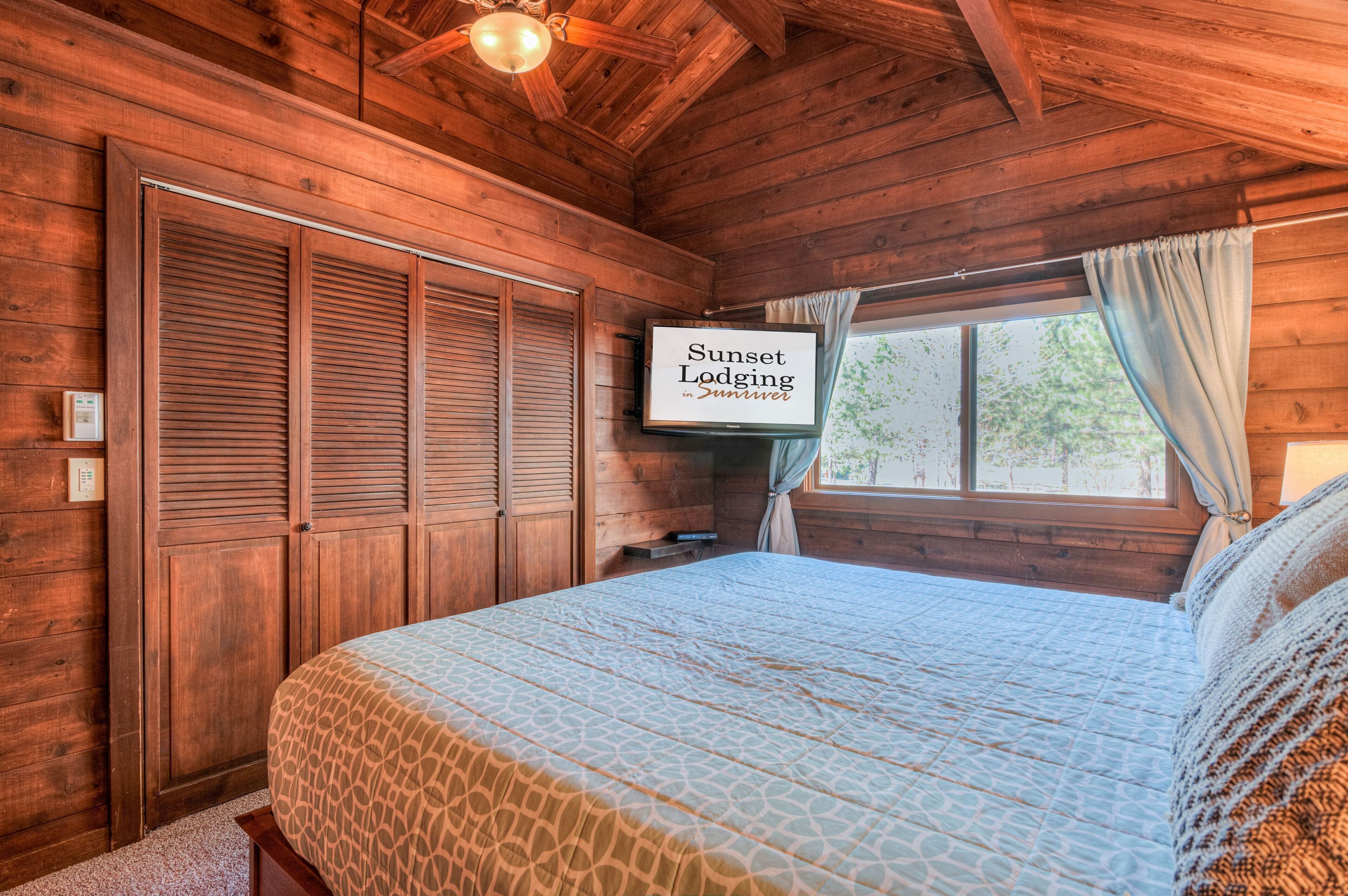Une chambre dans un chalet en bois, avec un lit, une télévision et une fenêtre avec des rideaux.