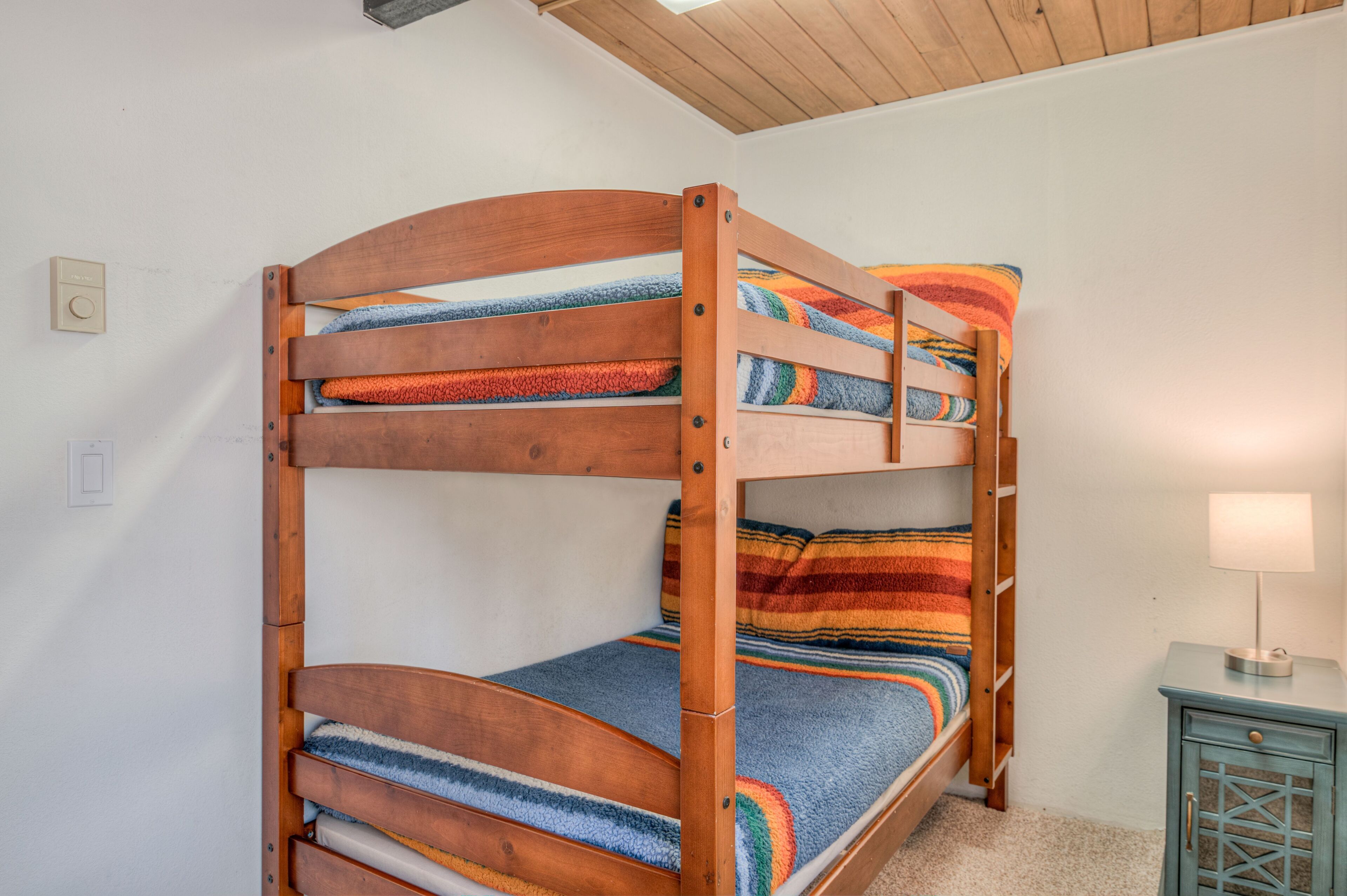 A bunk bed with wooden frames and colorful striped bedding.