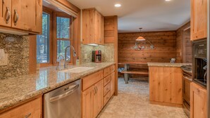 A kitchen with wooden cabinets, granite countertops, stainless steel appliances, and a window with a view of trees.