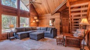 A log cabin interior with a large sectional sofa, a wooden chair, and a ceiling fan.