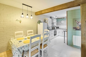 Uma sala de jantar com uma mesa posta para quatro pessoas, uma cozinha ao fundo e um relógio na parede.