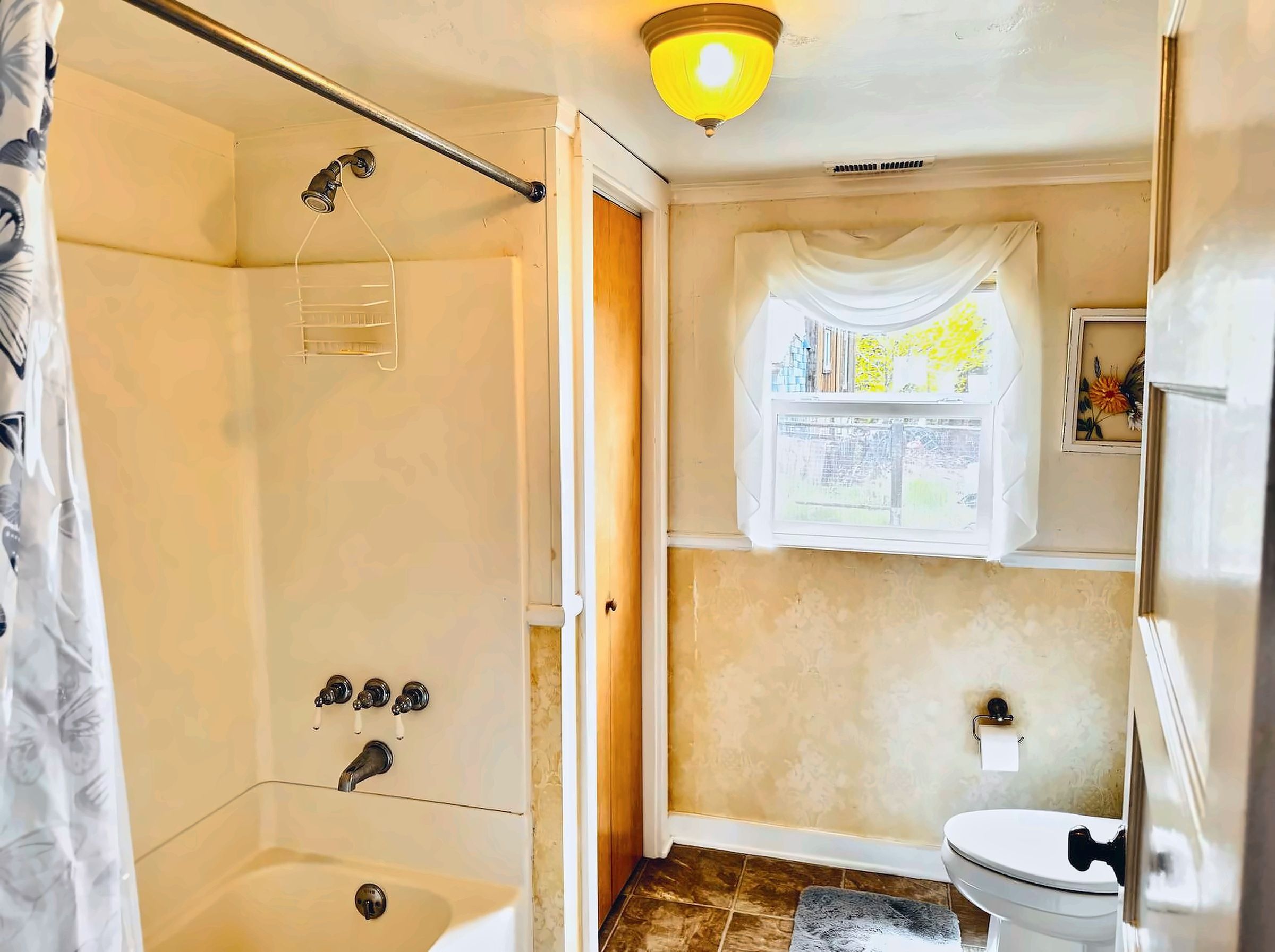 Un baño con ducha, inodoro y ventana con cortinas.