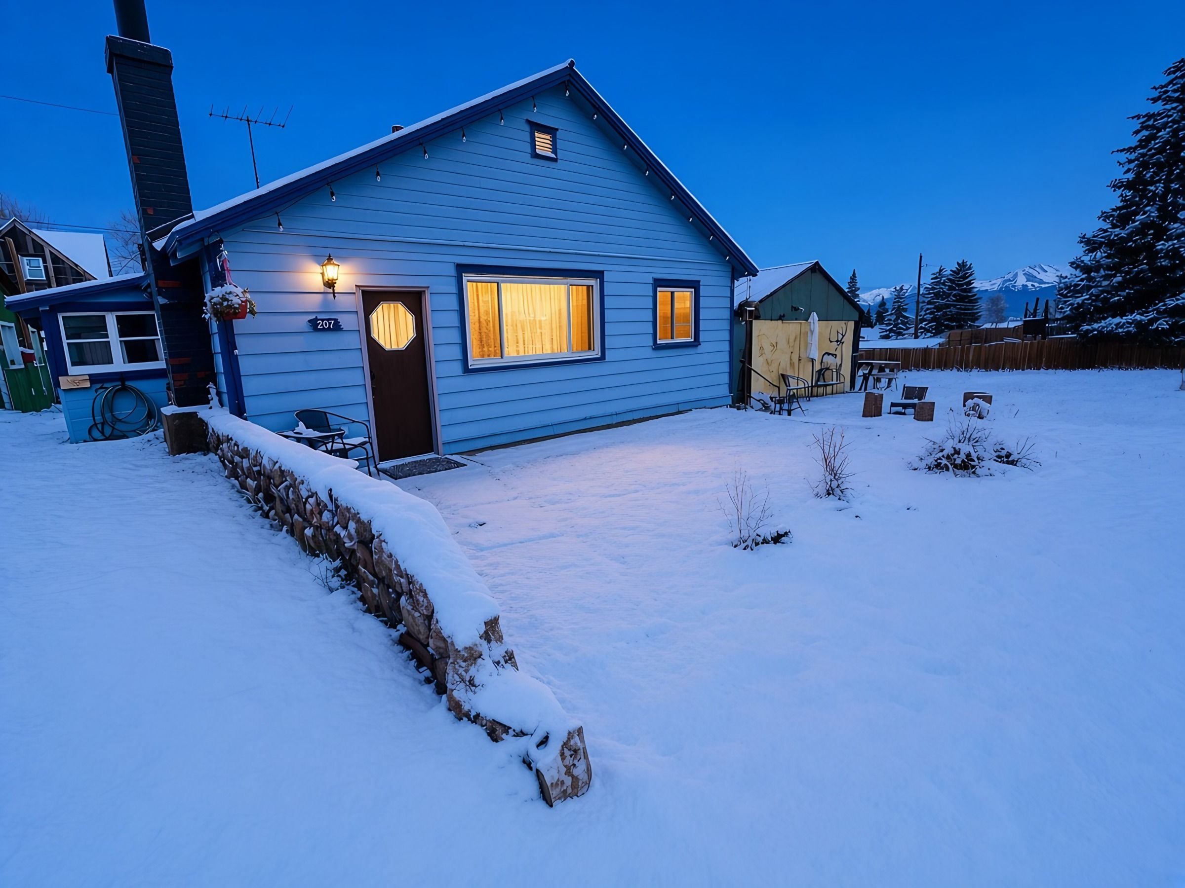 Una casa azul con la puerta y ventanas delanteras iluminadas, rodeada de nieve.