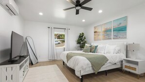 A bedroom with a bed, a TV, a ceiling fan, a window with curtains, and artwork on the wall. - 4BR | Hilltop House Sunset Cliffs | Beach, Bars, Ocean View (San Diego)