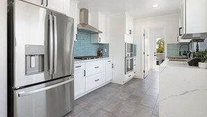A modern kitchen with stainless steel appliances, white cabinetry, and a blue-tiled backsplash. - 4BR | Hilltop House Sunset Cliffs | Beach, Bars, Ocean View (San Diego)