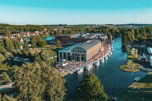 A riverside building with a large glass facade, surrounded by a dock with boats, and a park area with people. - Charming Swedish Forest Cottage Motala (Motala)