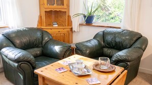 A room with two black leather armchairs facing each other, a wooden coffee table with teacups and saucers, and a wooden cabinet with a potted plant on a windowsill. - Charming Swedish Forest Cottage Motala (Motala)