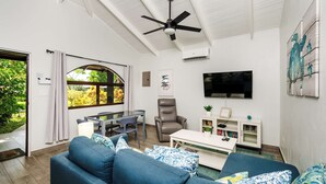 A living room with a blue sofa, a dining table, a TV, and a ceiling fan. - Jungle Villa, Pool, Private Patio & Concierge (Playa Potrero)