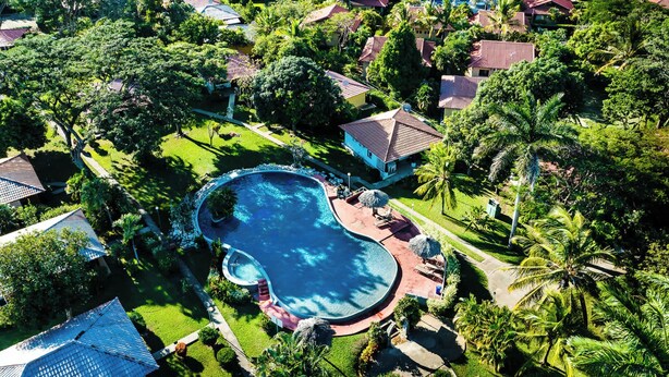 An aerial view of a resort with a large swimming pool, surrounded by lush greenery and multiple villas with red roofs. - Jungle Villa, Pool, Private Patio & Concierge (Playa Potrero)