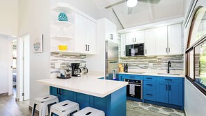 A modern kitchen with white and blue cabinetry, a central island with stools, a microwave, and a refrigerator. - Jungle Villa, Pool, Private Patio & Concierge (Playa Potrero)