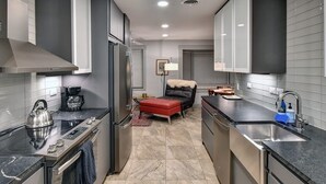 Una cocina moderna con estufa, refrigerador y pileta. Se ve un pouf rojo y una lámpara al fondo.