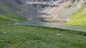 Un paisaje montañoso con un lago y zonas de pasto.