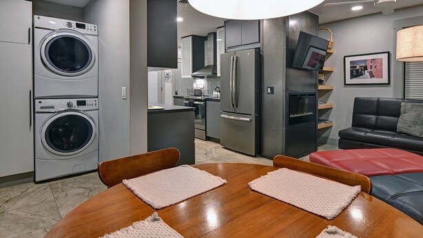 Una cocina moderna con electrodomésticos integrados, una zona de comedor con mesa y sillas de madera, y un salón con sofá y televisor.