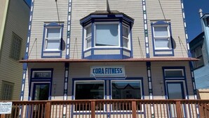 Un edificio con un cartel que dice "CORA FITNESS" y un balcón con barandilla de madera.