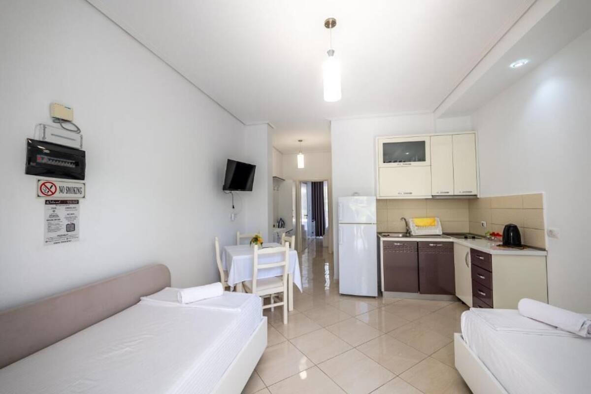 Une chambre d’hôtel avec deux lits, une petite table à manger, un coin cuisine équipé de placards et d’un réfrigérateur, et un téléviseur fixé au mur.