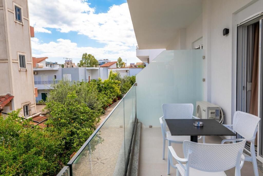 A balcony with a table and chairs, overlooking a garden and neighboring buildings.