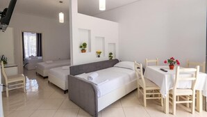 Een moderne, goed verlichte kamer met een grijze bank, een eettafel met stoelen en een kleine keukenhoek.