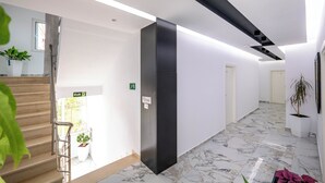 Een moderne hotelgang met marmeren vloeren, een trap met metalen leuningen en kamerplanten.