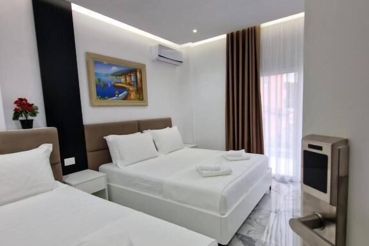 Une chambre d’hôtel avec deux lits, un tableau au mur, un climatiseur, une télévision et un sol en marbre.