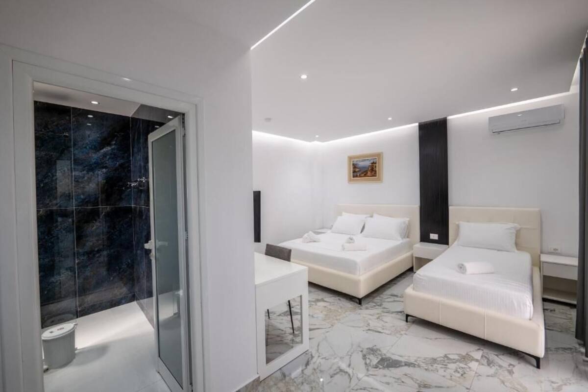 Une chambre d’hôtel moderne avec deux lits, une douche en verre et un sol en marbre.