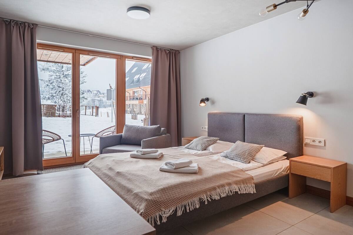 Egy modern szállodaszoba, amelyben egy nagy ágy, egy íróasztal található, és kilátás nyílik a hóval borított kültéri területre.