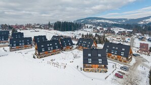 Un pueblo cubierto de nieve con casas de madera modernas, una pista de esquí y una vista despejada de las montañas circundantes.