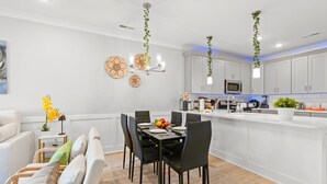A modern kitchen with white cabinets, a central island, and hanging plants.