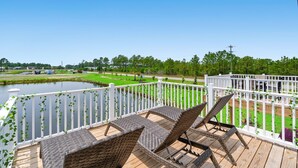 A deck with wicker chairs and a view of a pond and greenery.