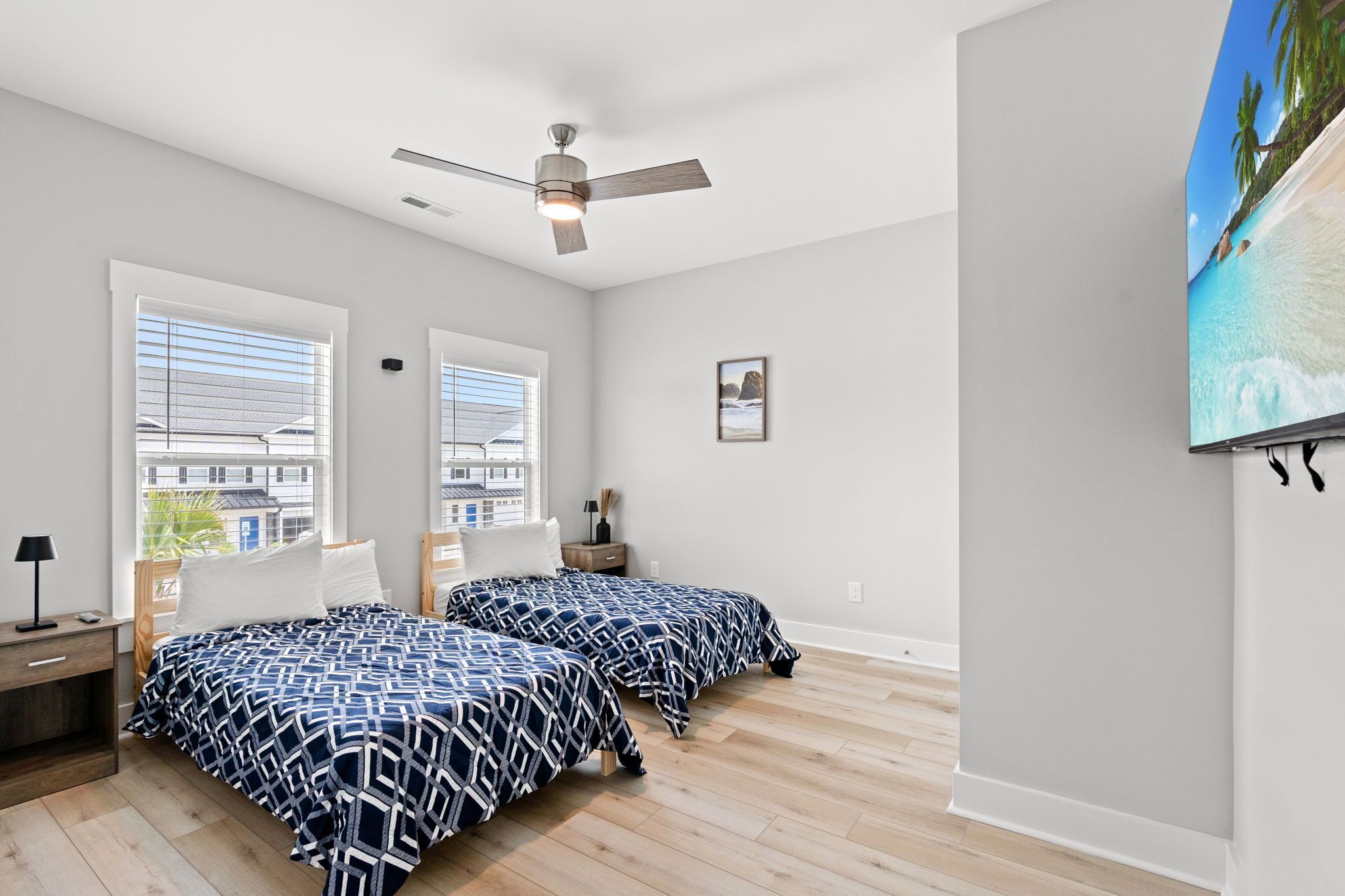 A bedroom with two beds, a ceiling fan, a large window, and a painting on the wall.