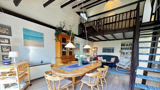 A rustic dining area with a wooden table and chairs, a hanging light fixture, and a bookshelf filled with books. - Pet-free vacation home on the North Sea (Ellemeet)