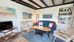A modern living room with a TV, seating, a coffee table, and a bookshelf. - Pet-free vacation home on the North Sea (Ellemeet)