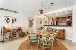 A dining area with a round glass table, wicker chairs, and a hanging light fixture.